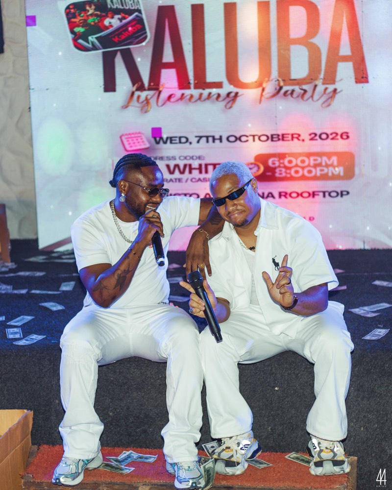 Two guests seated on stage in front of the event artwork, showing the date, dress code, time and venue.